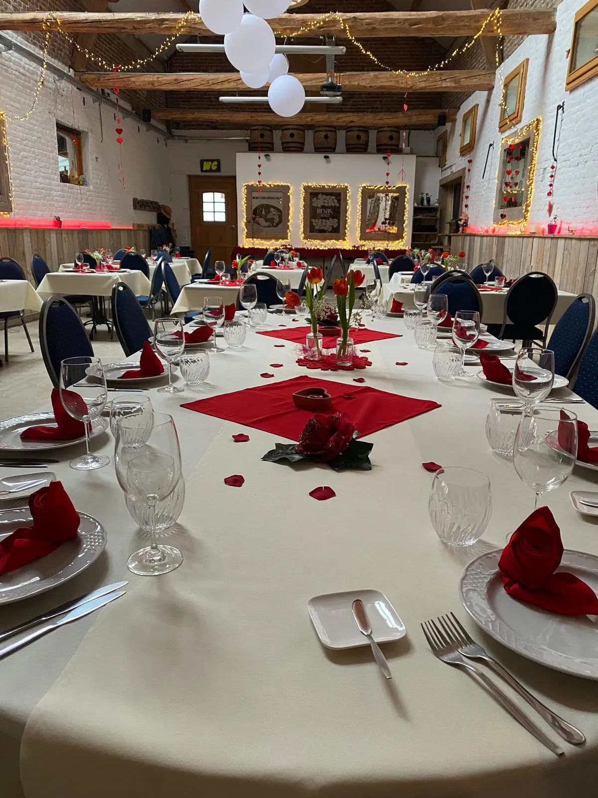 Gedekte feesttafel met wit tafellinnen, rode servetten en rozen