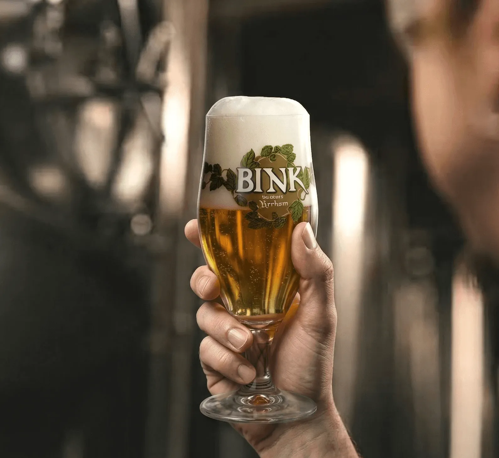 Een hand houdt een vol glas Bink-bier vast
